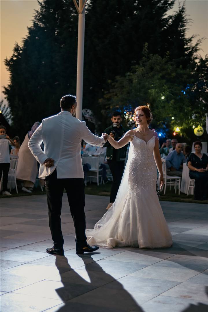 A bride and groom share their first dance on an outdoor dance floor at dusk